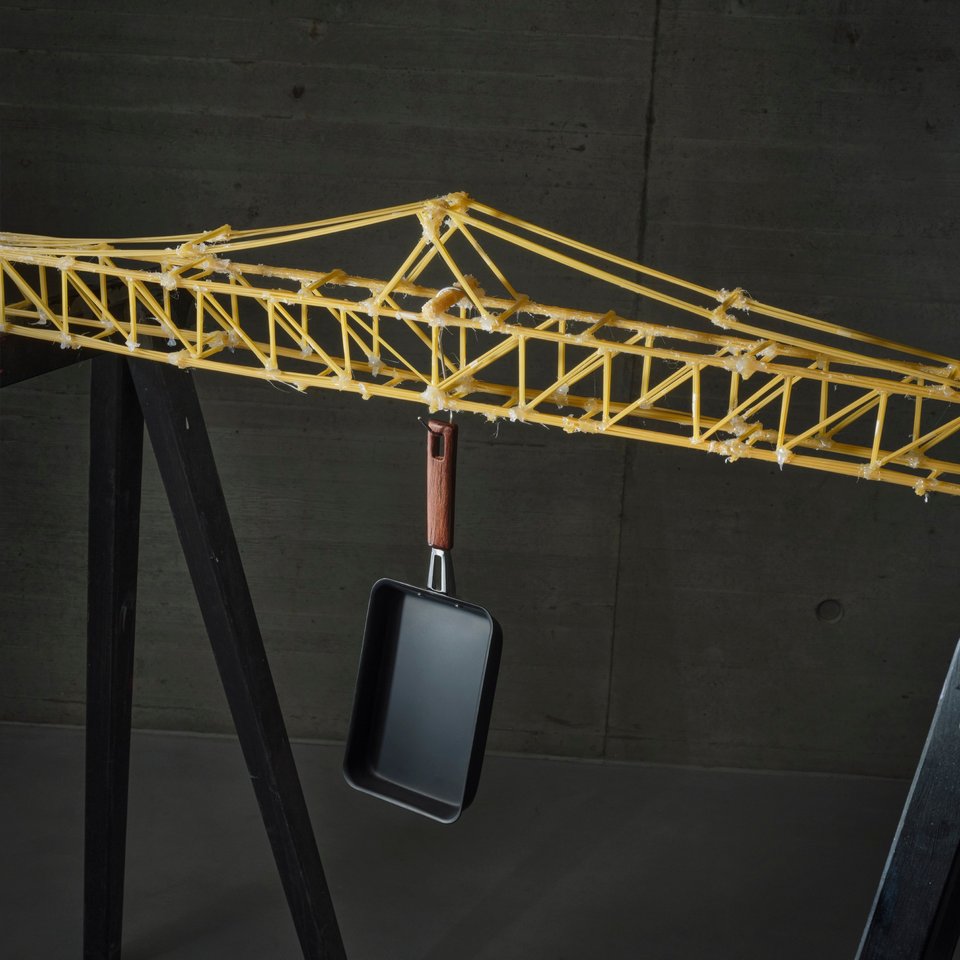 Darstellung einer Brücke aus Spaghetti, an der eine Pfanne hängt