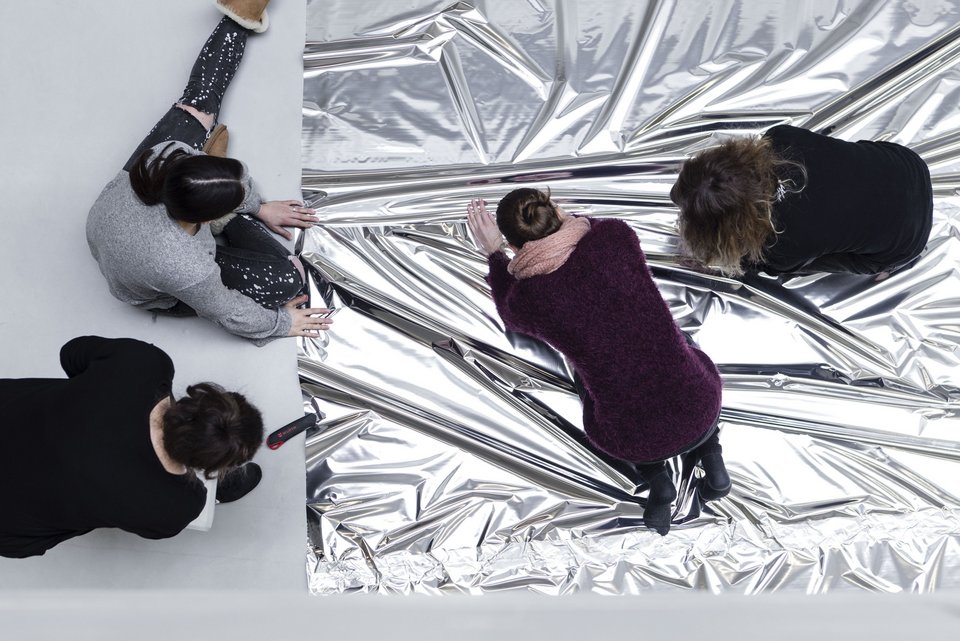 Vier Studierende sitzen auf dem Boden und bearbeiten eine silberne Folie